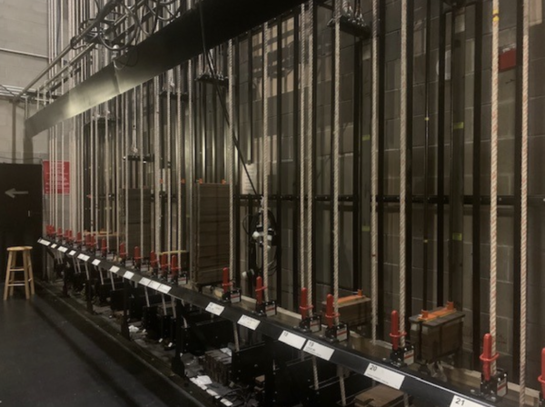 202408-Screen-Shot-2024-08-30-at-9.34.31-AM-600x448 Backstage view of a theater fly rail system with rows of ropes, pulleys, counterweights, and locking mechanisms used to raise and lower scenery, curtains, and lighting above the stage.