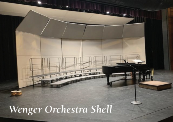 202509-Screen-Shot-2025-09-09-at-1.52.11-PM-600x424 Concert choir setup on a theater stage featuring a curved Wenger orchestra shell, tiered choral risers, a grand piano, microphone stand, and conductor’s podium beneath stage lighting. Text in the lower corner reads: ‘Wenger Orchestra Shell.